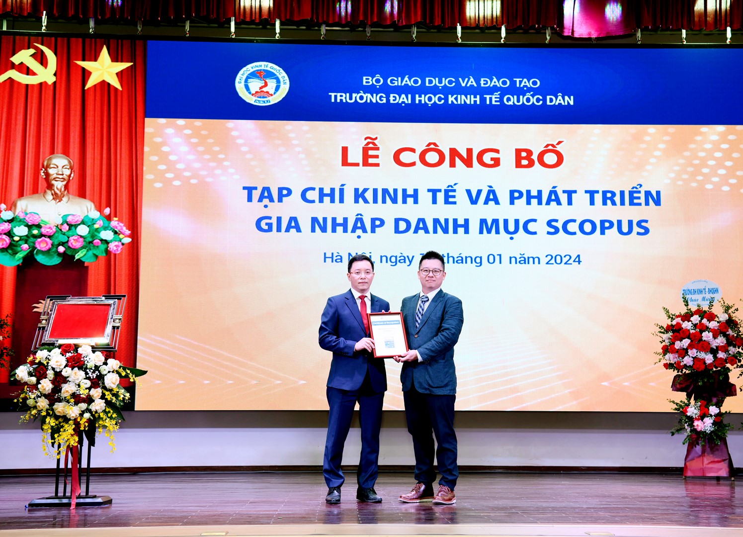 Two men standing on a stage holding a certificate  Description automatically generated